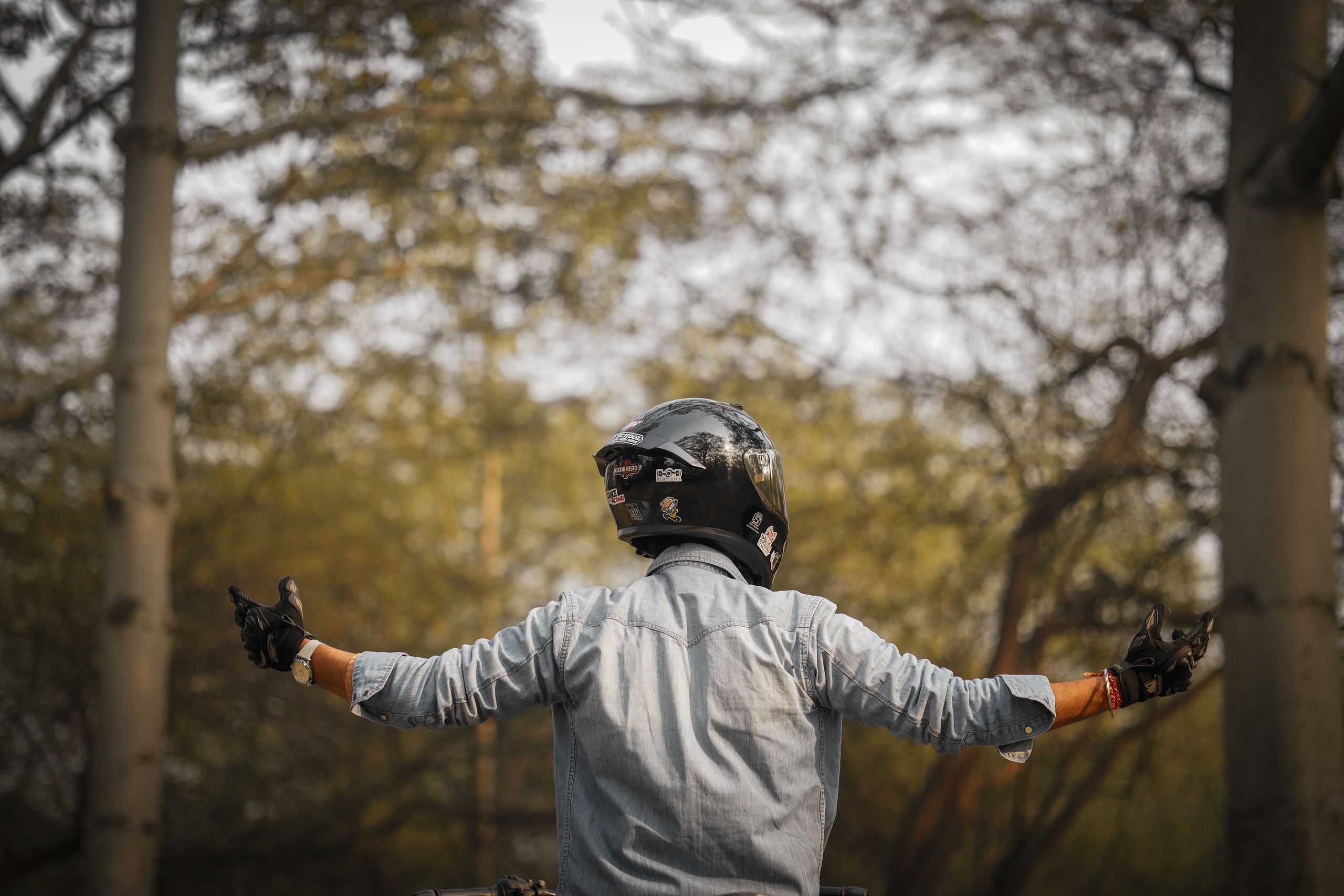 A motorcyclist wearing a helmet and gloves enjoys the tranquility of a forest environment.