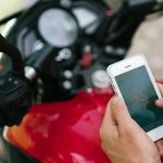 From above of crop unrecognizable tattooed male using smartphone while studying map of city via app in Internet sitting on motorbike on street